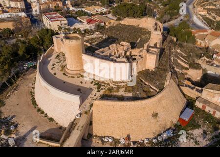 Aerial panoramic view of medieval Elda castle above the town with partially restored walls, towers and gate made of white lime stone in Spain Stock Photo
