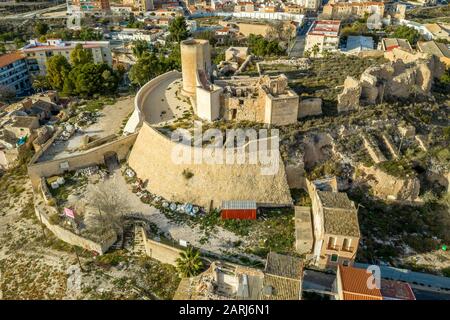 Aerial panoramic view of medieval Elda castle above the town with partially restored walls, towers and gate made of white lime stone in Spain Stock Photo