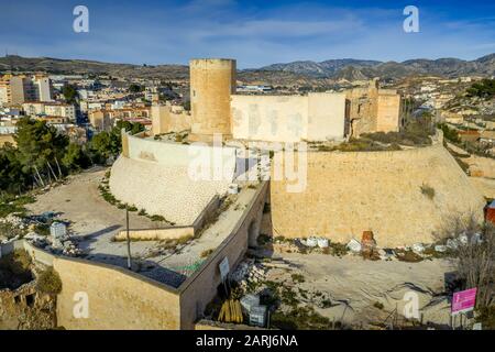 Aerial panoramic view of medieval Elda castle above the town with partially restored walls, towers and gate made of white lime stone in Spain Stock Photo