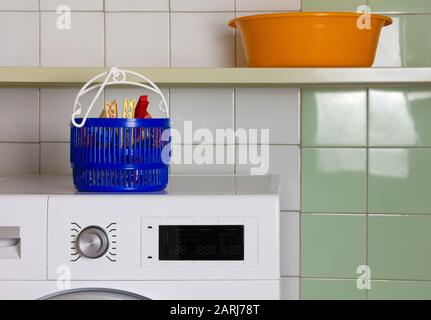 A basket for clothespins on the top of a washing machine and a wash bowl on the shelf in a laundry room Stock Photo