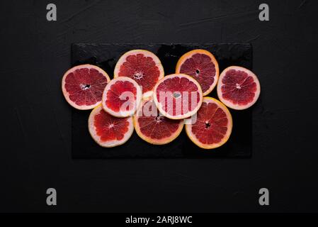 Juicy grapefruit slices on a black cutting board on a black table. Above view of sliced grapefruit. Summer  fruits. Breakfast table setting. Stock Photo