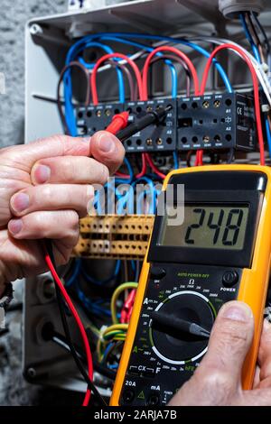 Electrician with multimeter tester measures the voltage in a residential distribution electrical panel. Construction industry, electrical system. Stock Photo