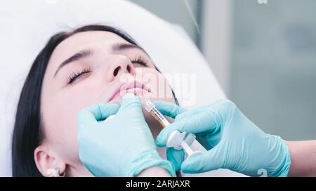 Beautician hands making botox injection in female lips. The doctor cosmetologist makes lip augmentation procedure. Concept of beauty salon and plastic Stock Photo