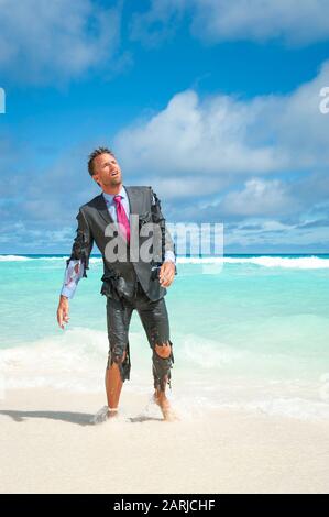 Survivor castaway businessman washed up on a tropical beach in a ragged torn suit Stock Photo