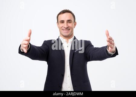 Overjoyed happy man in suit standing with his hands wide open welcoming his parners or friends. Studio shot Stock Photo