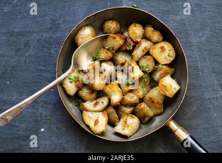 Roasted Jerusalem Artichokes in a pan on a slate background. Stock Photo