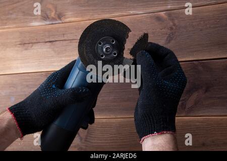 Grinder with a broken blade in the hands of working gloves on a wooden table. Danger of using a power tool Stock Photo