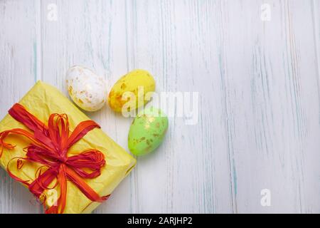 Easter background. Easter multi-colored eggs, gift box on a light wooden background with a place for copy space. Stock Photo
