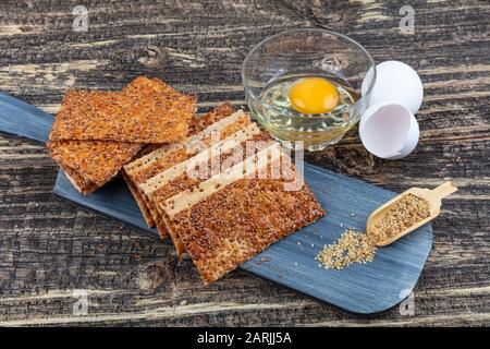 Various crispy wheat, rye and corn flatbread crackers with sesame  seeds on rustic grey wooden background. Top view point. Stock Photo
