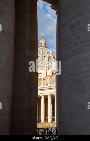 A view of St. Peters Basilica between the pillars of the colonnade around St. Peters Square, Vatican City. Stock Photo