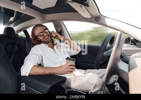 Young adult man sitting in car, talking on smartphone Stock Photo
