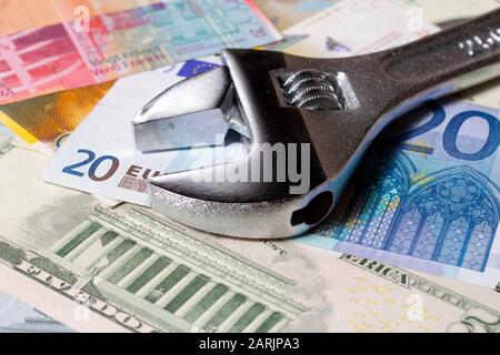 Adjustable wrench on a stack of various Euro, US dollar and Swiss franc banknotes. Stock Photo