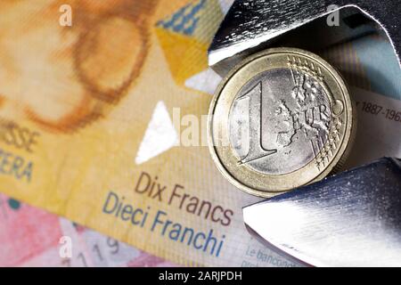 One euro coin in an adjustable wrench on Swiss franc banknotes. Stock Photo