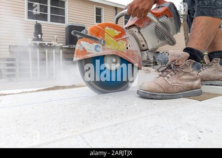 construction worker, brick layer, paver cutting a tile on the pooldeck of a  residence using a heavy duty stone saw creating dust. Stock Photo