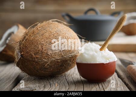 Healthy coconut oil for cooking in ceramic bowl and coconuts on wooden kitchen table. Stock Photo