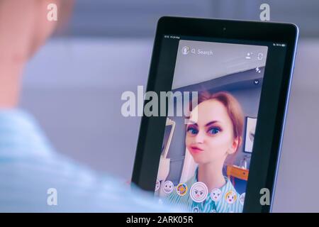 Woman using Snapchat multimedia messaging app with face mask on tablet Stock Photo