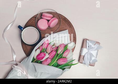 Coffee cup, spring tulip flowers and pink macarons on wooden table top view. Greeting for Womans or Mothers Day Stock Photo