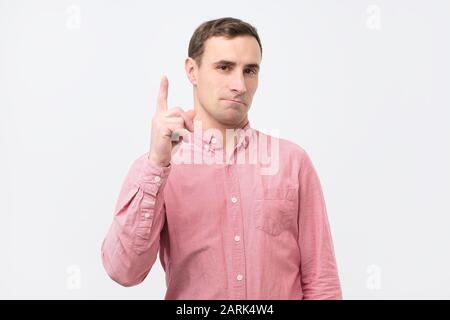 Clever young man in pink shirt pointing up by finger warning you from making a mistake. Studio shot Stock Photo