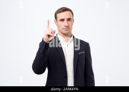 Clever young man in suit pointing up by finger giving advice to his partner or coworker. Studio shot Stock Photo