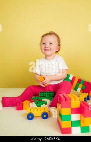 Caucasian little girl, children isolated on yellow studio background. Portrait of cute and adorable kid, baby playing and laughting. Concept of childhood, family, happiness, new life, education. Stock Photo