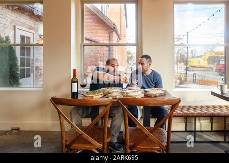 Two men share a meal an bottle of wine together in an empty restaurant Stock Photo