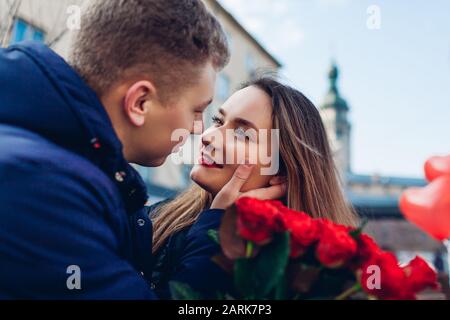 Valentines day date. Man and woman about to kiss outdoors. Couple walking with roses flowers and balloons Stock Photo