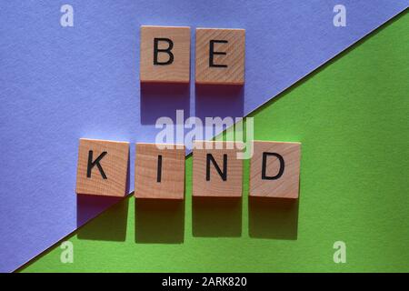 Be Kind, words in 3d wooden alphabet letters on a mauve and green background Stock Photo