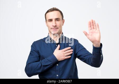Swear to say truth. Sincere happy man raising palm and holding hand on chest, promising to me honest Stock Photo