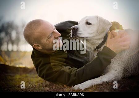 Young adult man lying on the grass with his dog at sunset. Stock Photo