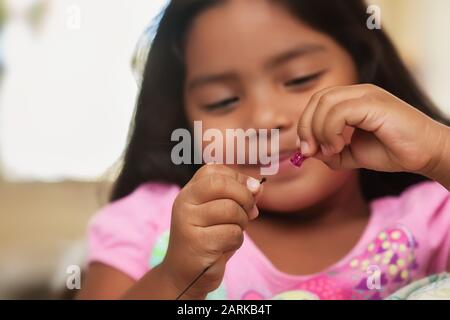 A cute little girl having fun while while creating bead jewelry using string and colorful beads. Stock Photo