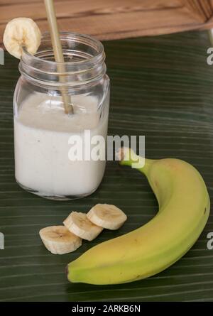 closeup of banana milkshake with a banana and slices on green banana leaf Stock Photo