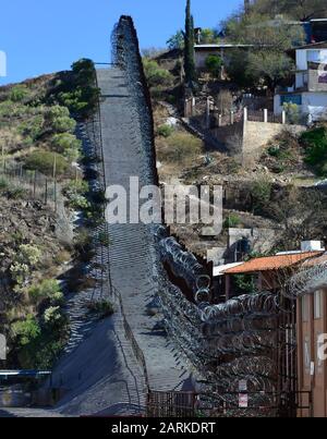 View of US/Mexico metal international border fence with razor wire following uphill with Mexican houses on other side of fence from Nogales, AZ, USA Stock Photo
