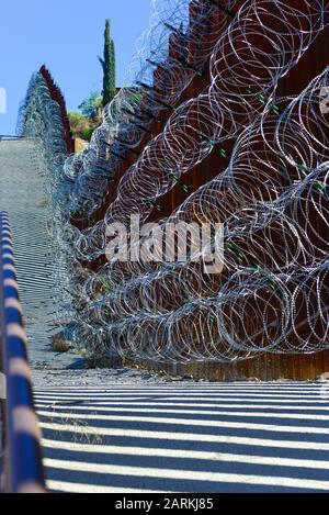 View of US/Mexico metal international border fence with razor wire following uphill between Nogales, AZ, USA and Nogales, Sonora, MX, Stock Photo