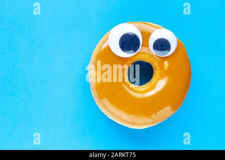 A Canadian Maple Dip Donut with Black Wiggle Googly Eyeballs on a blue background Stock Photo