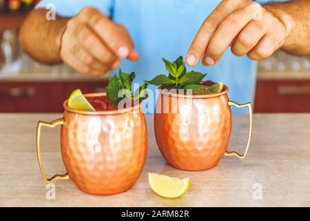Barman is decorating Moscow mule cocktails in metallic cups with lemon and mint. Party concept. Stock Photo