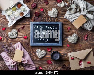 Zero waste Valentine's Day concept. Eco-friendly gift cloth wrapping in Furoshiki style, homemade sweets as gift ideas and chalkboard with Zero Waste Valentine's Day letters on brown wooden background Stock Photo