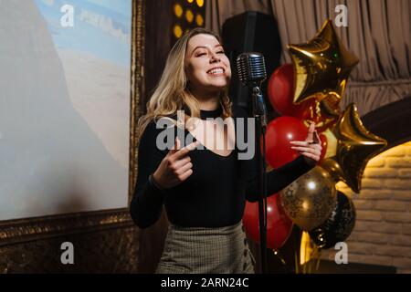 A beautiful young girl very energetically performs a beautiful karaoke song in a nightclub. Stock Photo