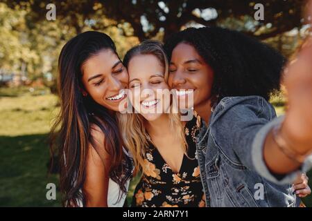 Close up portrait of smiling multiracial millennial women laugh stand posing for group picture together - Group of friends taking a selfie outdoors in Stock Photo