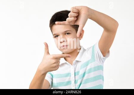 happy funny little child boy in striped t-shirt making hands photo frame gesture on white background. facial expression Stock Photo