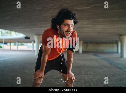 Portrait of sweaty and tired young male fit person taking a break after jogging in city street under the bridge
