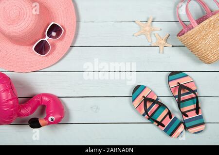 Flat lay with a summer holiday concept with blue wooden background an pink hat, sunglasses, flip flops and beach accessoires seen from a high angle Stock Photo
