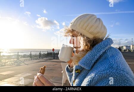 Mature middle aged woman enjoying a cup of coffee and cookie at a Brighton seafront cafe on winter sunny day Stock Photo