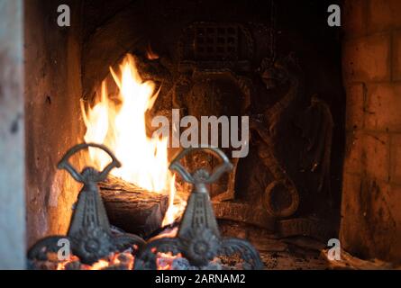 Fire burning in a dragon fireplace in an old house with the mystical beasts depicted on the metal back plate and andirons in the foreground Stock Photo