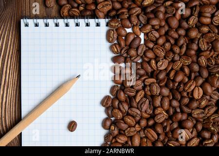 Roasted coffee beans with paper notepad and pencil. Top view. Close up. Stock Photo
