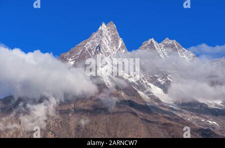 Sharp rocky peaks resembling the teeth of the saw on the background of blue sky; majestic peaks towering above the clouds Stock Photo