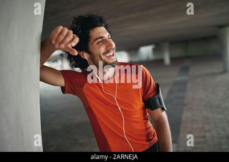 Portrait of healthy happy young caucasian man standing outdoors and looking away enjoying the music on earphones after running - happy runner  Stock Photo