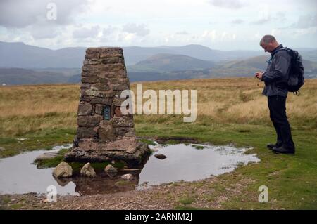 Man Checking GPS Compass by the Summit Cairn of the Wainwright 'Loadpot Hill' in the Lake District National Park, Cumbria, England, UK Stock Photo