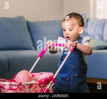 portrait of a cute little baby girl playing mothers and daughters with her pink doll in the buggy. Stock Photo