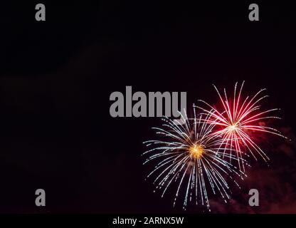 Two white with gold center starburst fireworks highlighted with red photographed against a black sky on the Fourth of July in Minnesota Stock Photo