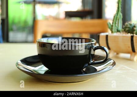 Black cup on wooden table with blurry coffee shop in background Stock Photo